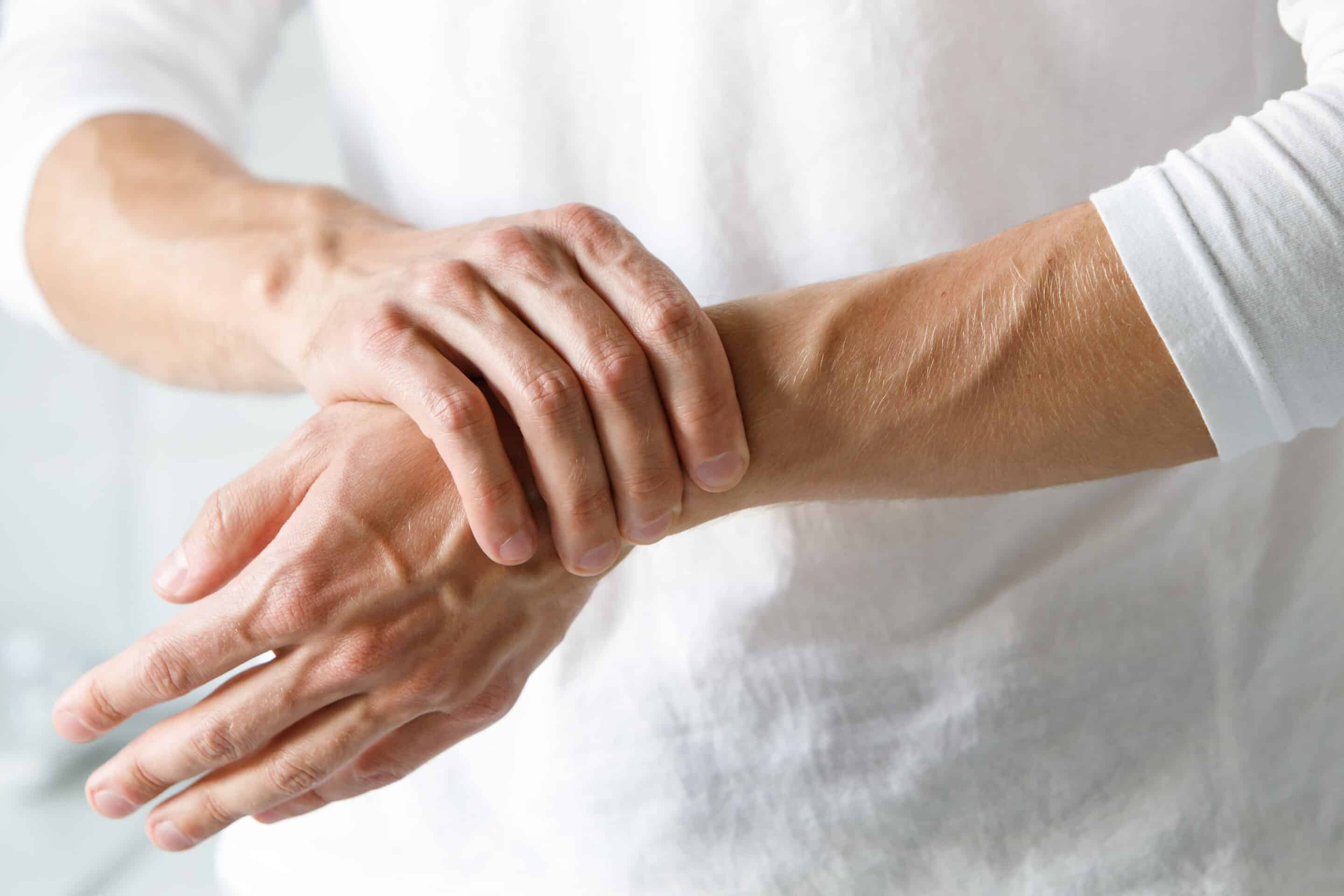 Closeup of male arms holding her painful wrist caused by prolonged work on the computer, laptop. Carpal tunnel syndrome, arthritis, neurological disease concept. Numbness of the hand